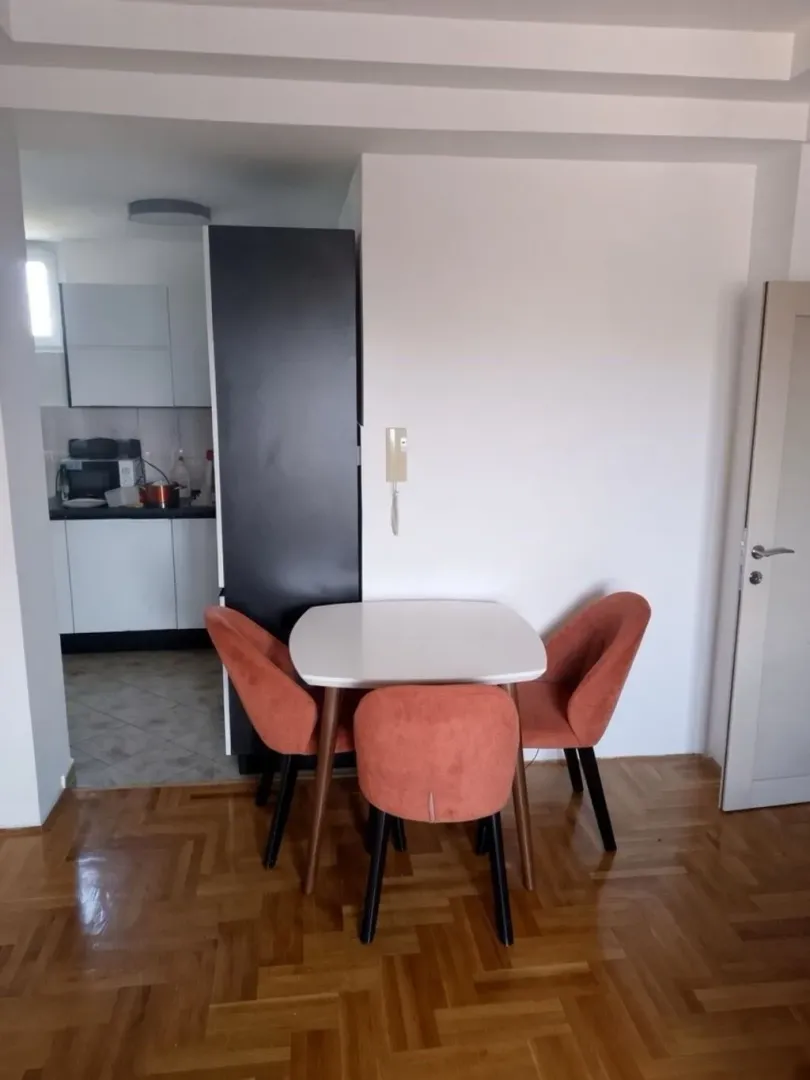 Trpezarijski sto sa narandžastim stolicama i pogledom na kuhinju.