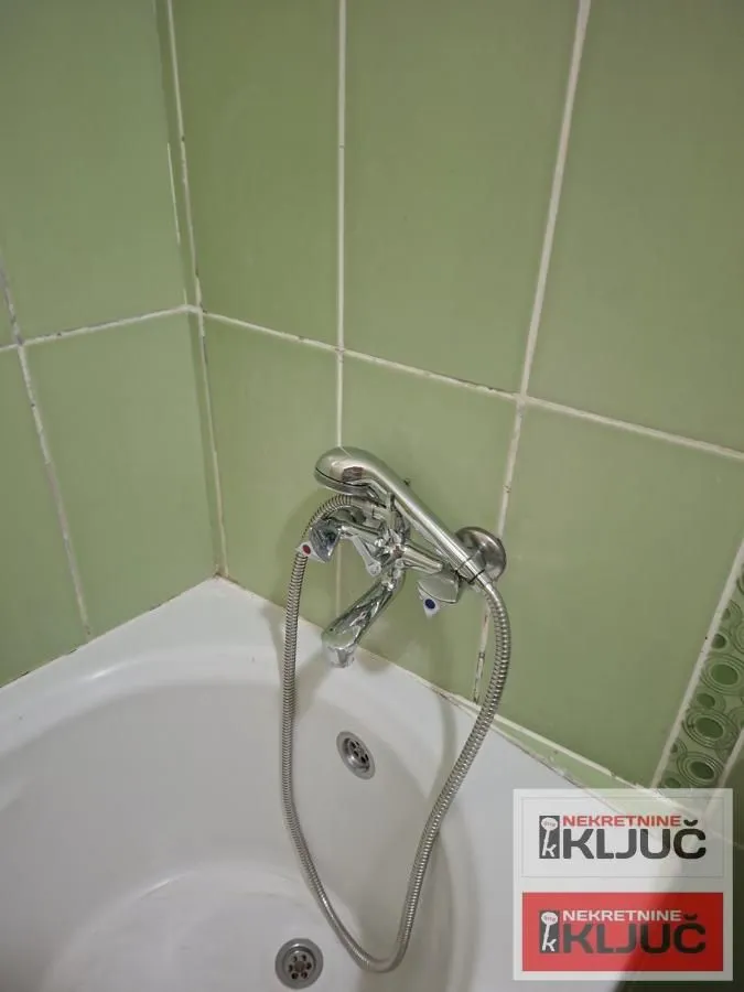 Pogled na kadu i slavinu u kupatilu obloženom zelenim pločicama.