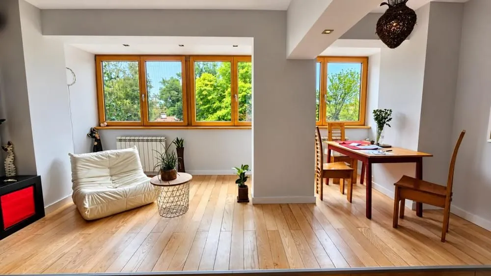 Bright living room with wooden flooring, an armchair, and a dining table.