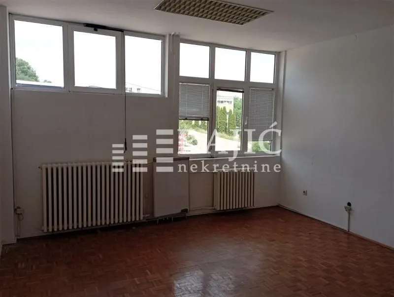 Empty room with parquet flooring and large windows.