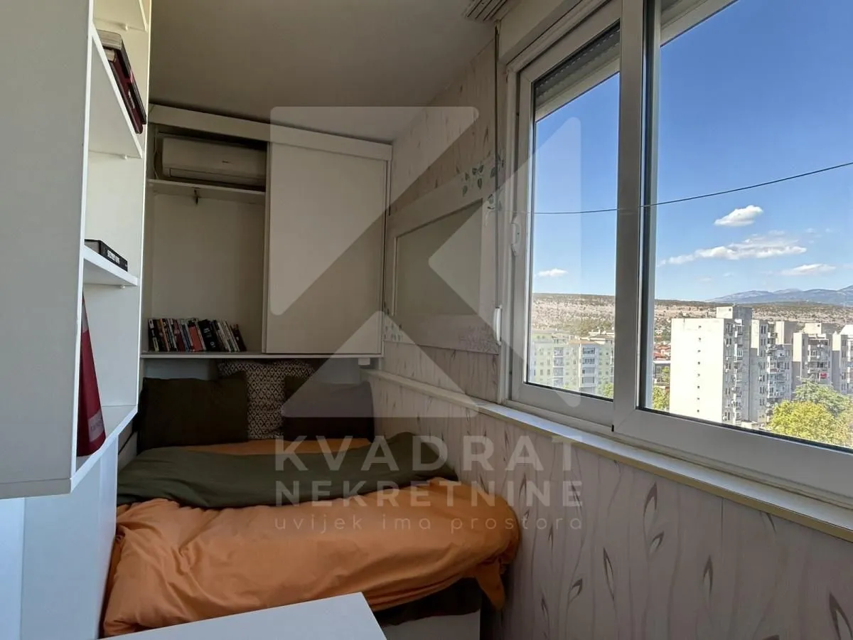 Smaller bedroom with a bed, shelves, and a large window.
