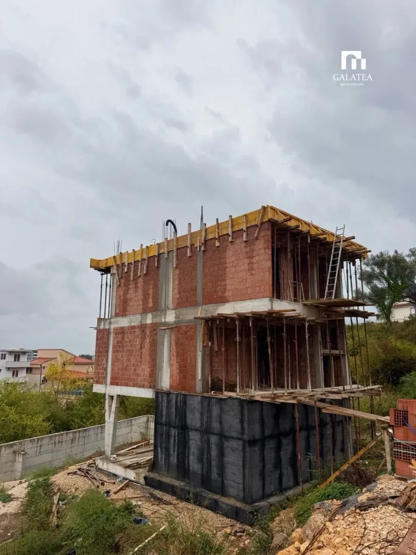 View of a house under construction with concrete structure and bricks.