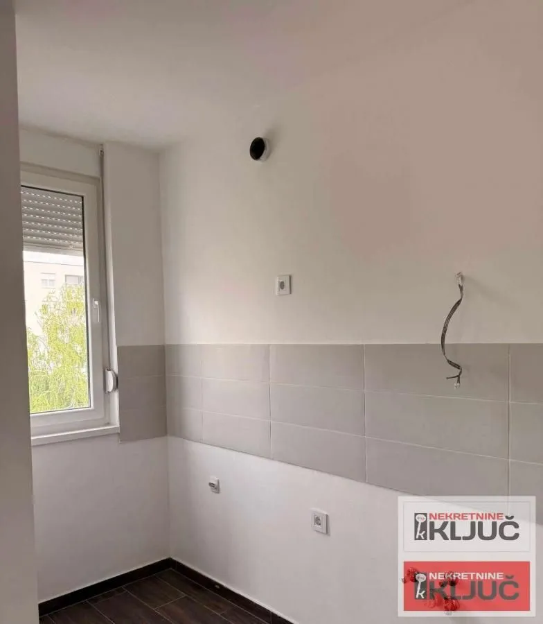 Prazna prostorija sa prozorom i keramičkim pločicama na zidu.