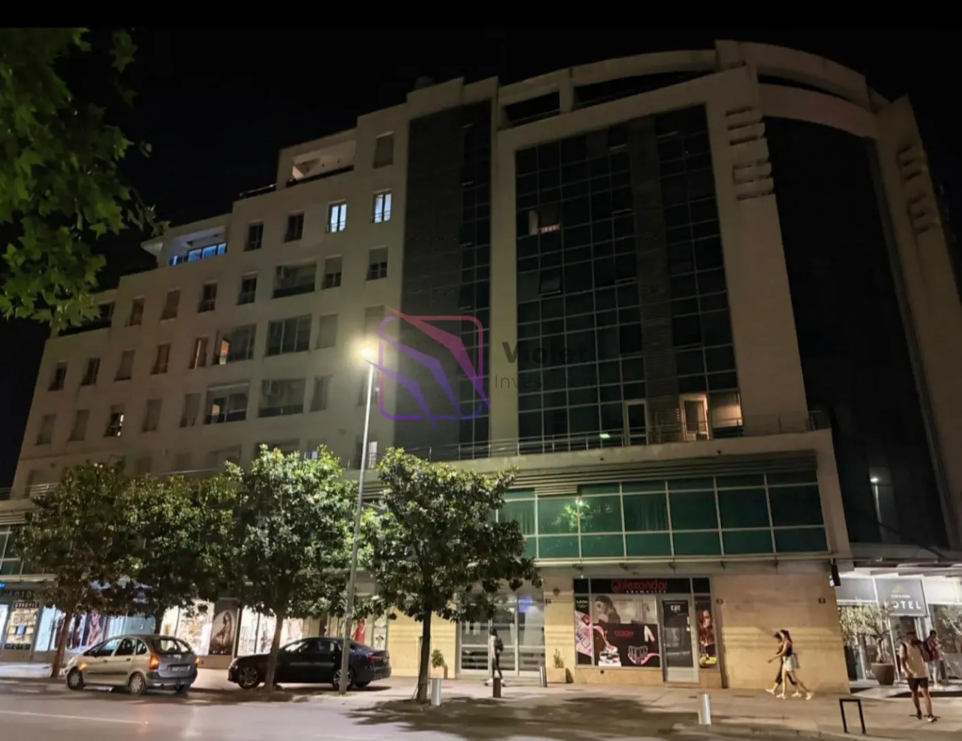 Noćni pogled na spoljašnjost višestambene zgrade sa poslovnim prostorima u prizemlju.