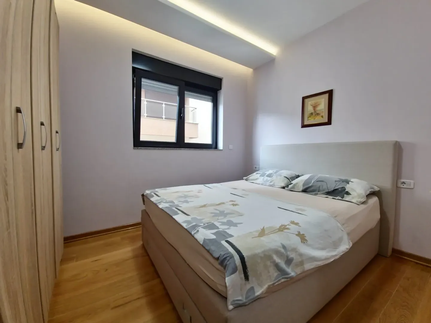 Spavaća soba sa bračnim krevetom, drvenim ormarom i prozorom.
