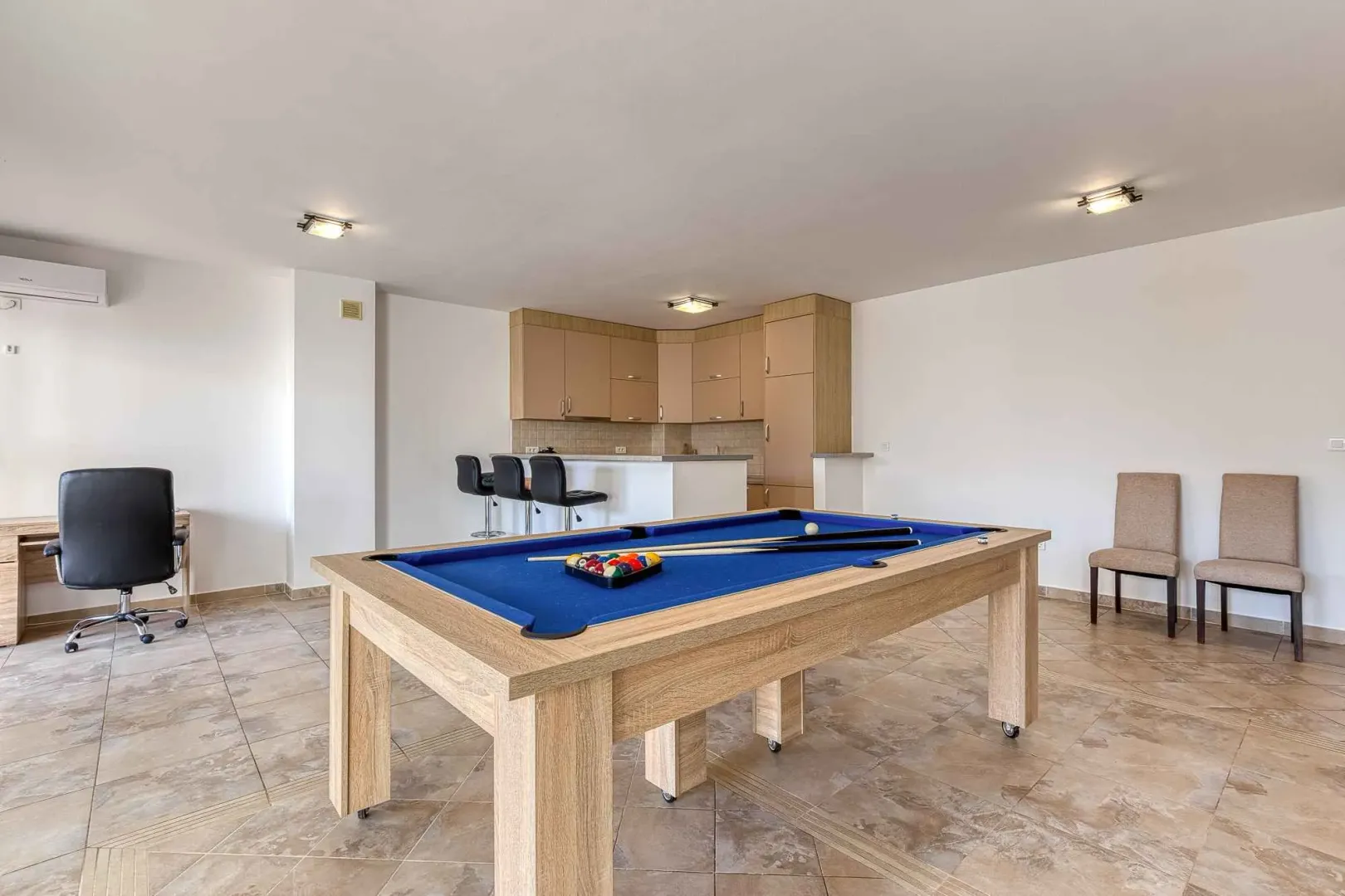 Spacious living room with a pool table and an open kitchen in the background.
