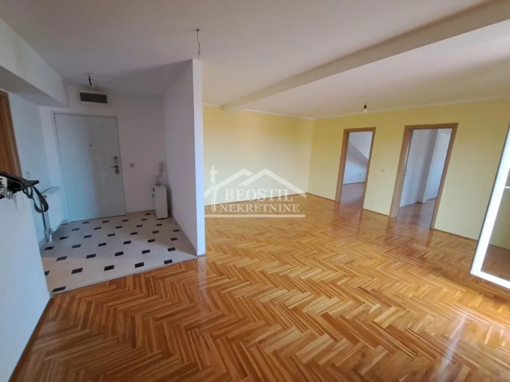 Prazan dnevni boravak sa parketom i ulaznim delom u stanu.