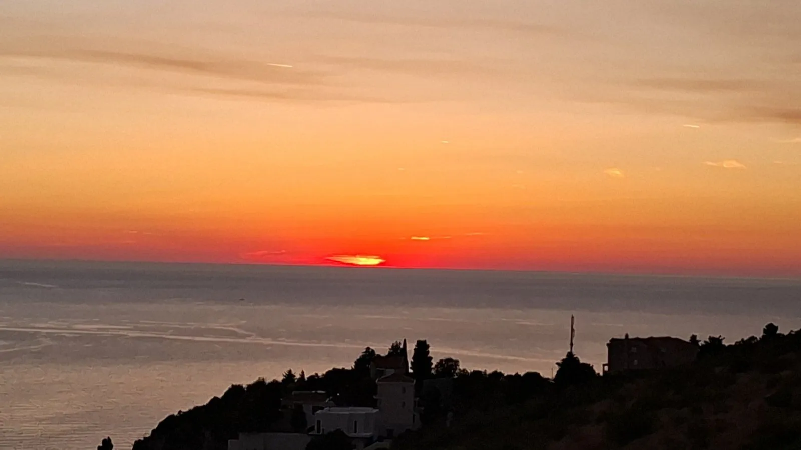 View of the sunset over the sea from a hill.