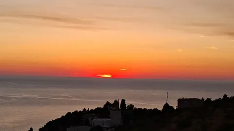 View of the sunset over the sea from a hill. - image 8