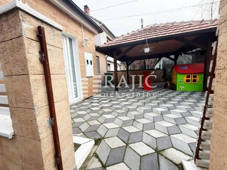 Popločano dvorište kuće sa natkrivenim letnjikovcem.