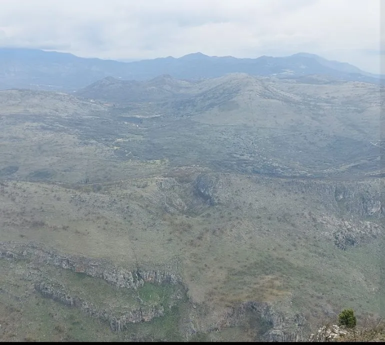 Panoramski pogled na brdoviti pejzaž i planine u daljini.