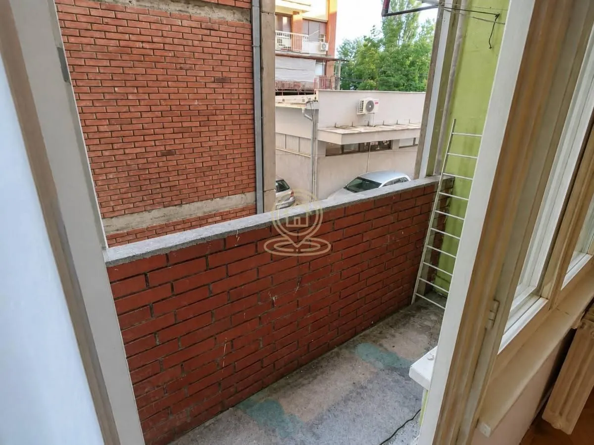 Manji nenamešten balkon sa ciglenom ogradom i pogledom na okolne zgrade i ulicu.