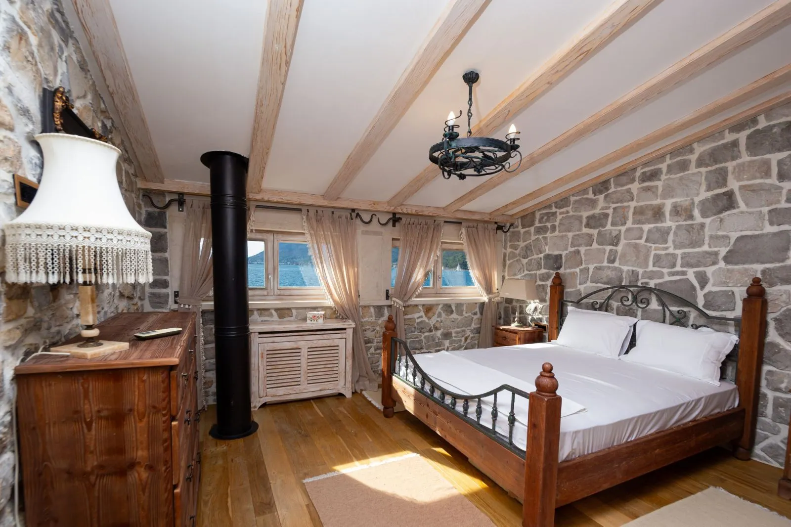 Rustic bedroom with stone walls, wooden beams, and a sea view.