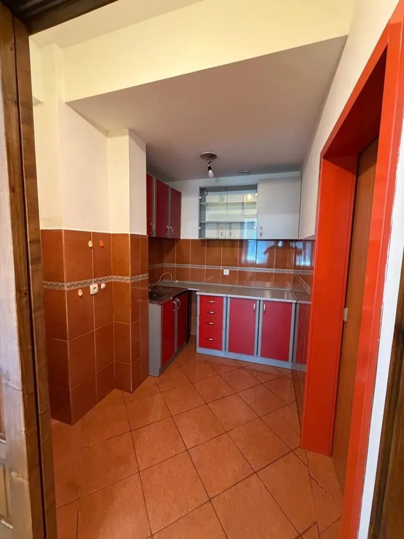 Smaller kitchen with red cabinets and brown ceramic tiles.
