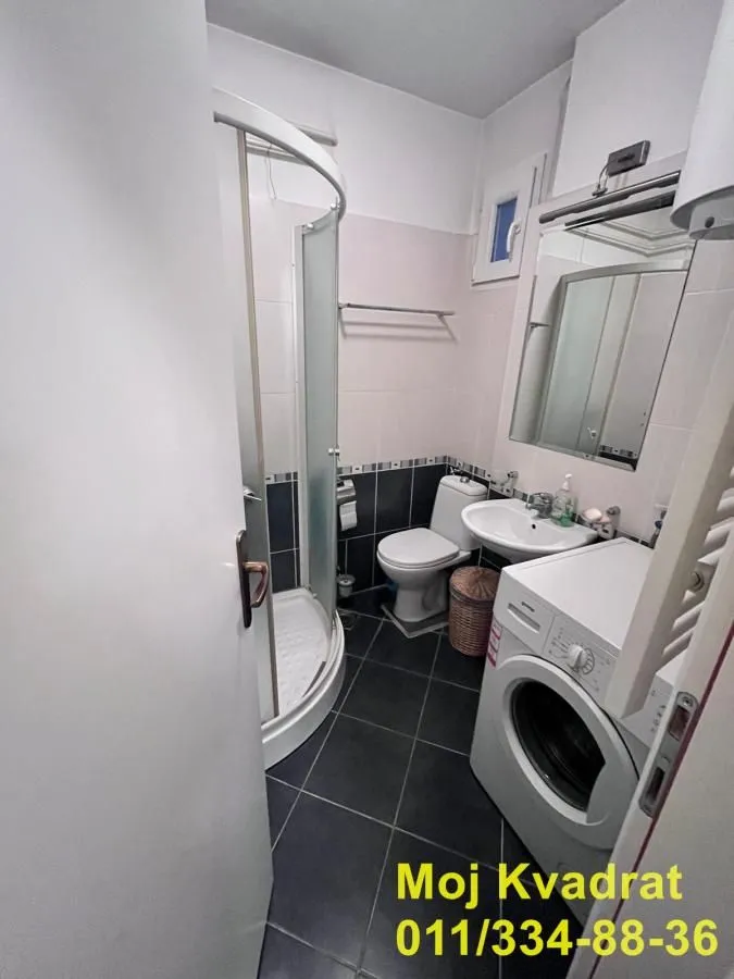 Manje kupatilo sa tuš kabinom, umivaonikom, WC šoljom i veš mašinom.