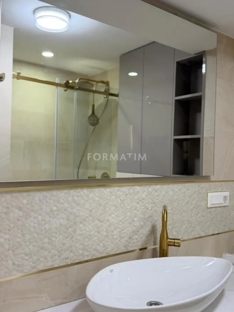 View of the sink with a gold faucet and mirror in a modern bathroom.