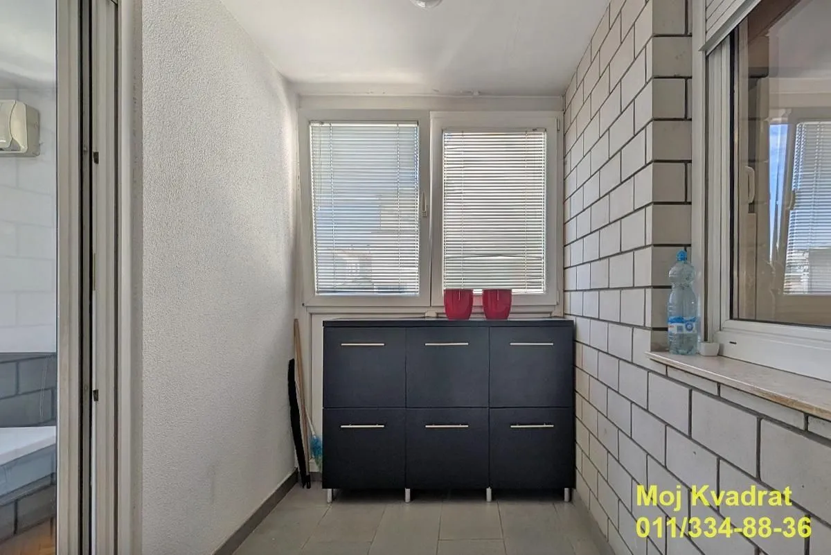 Enclosed balcony with a chest of drawers and windows with blinds.