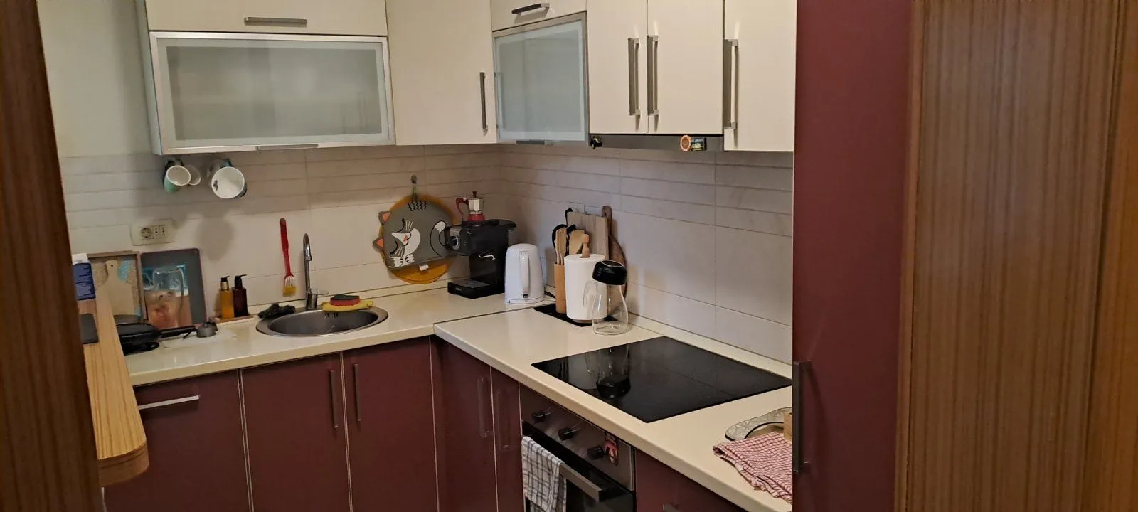 Compact equipped kitchen with white and dark red cabinets.