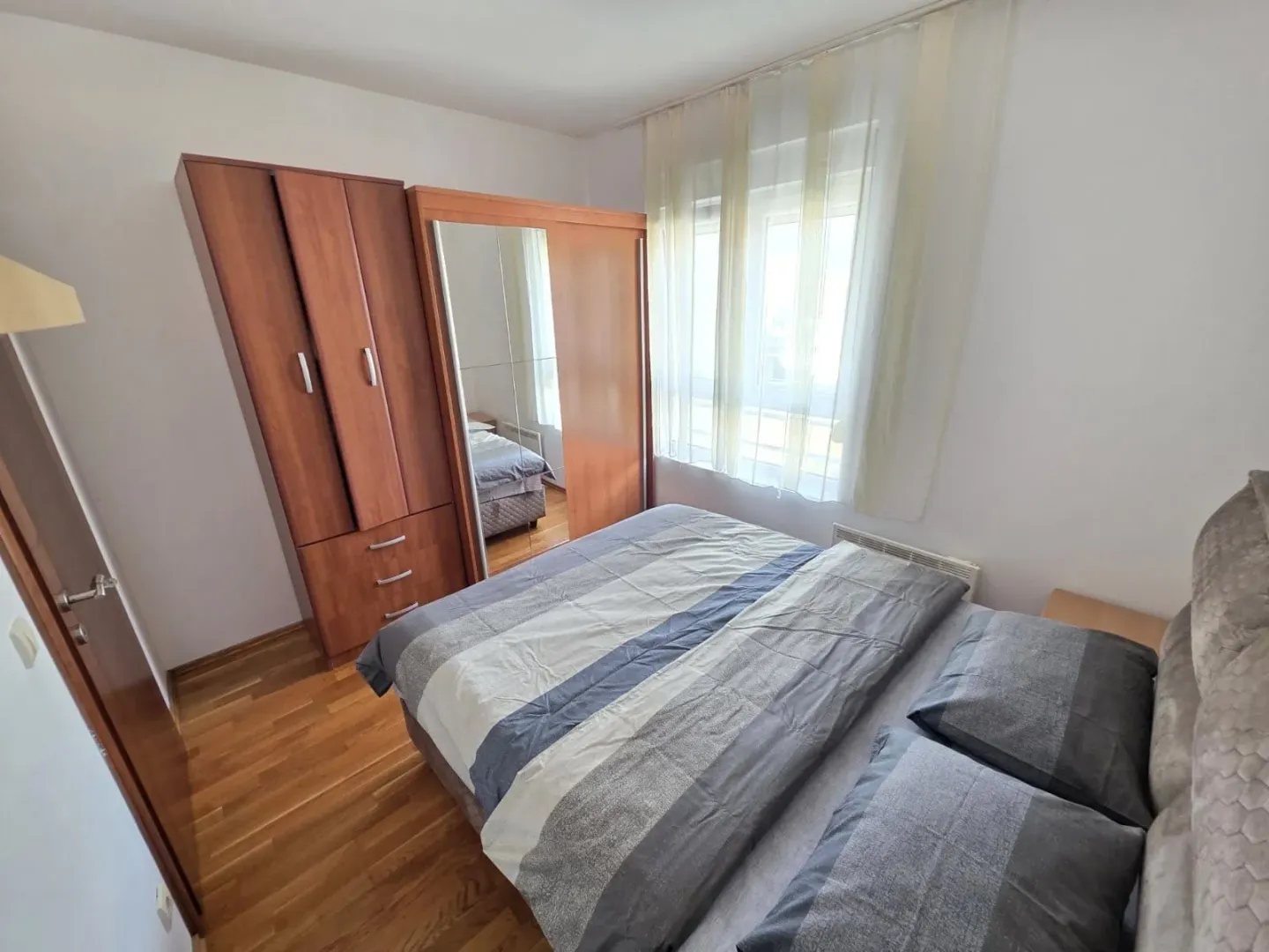 Namještena spavaća soba sa bračnim krevetom i drvenim ormarom.