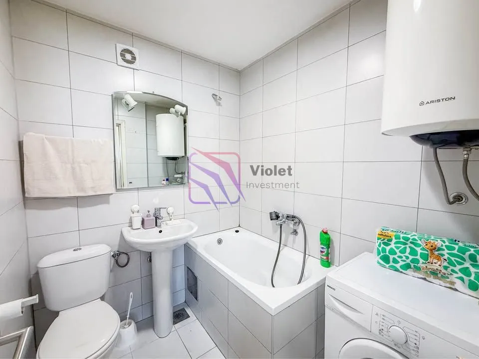 Small bathroom tiled in white with a bathtub, washbasin, toilet, and washing machine.