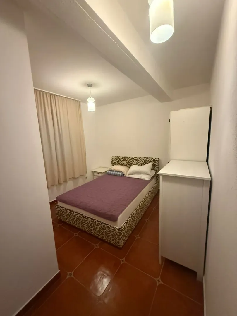 Manja spavaća soba sa bračnim krevetom, bijelim ormarom i prozorom sa zavjesom.