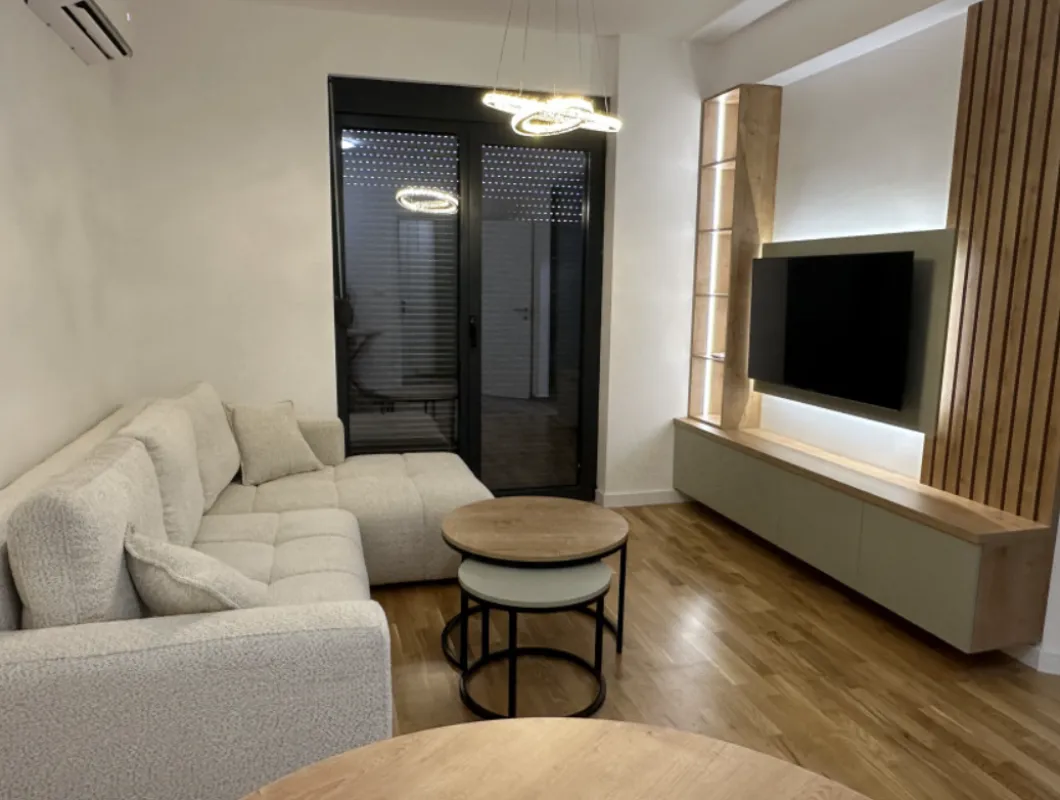 Moderan dnevni boravak sa ugaonom garniturom, TV komodom i izlazom na terasu.