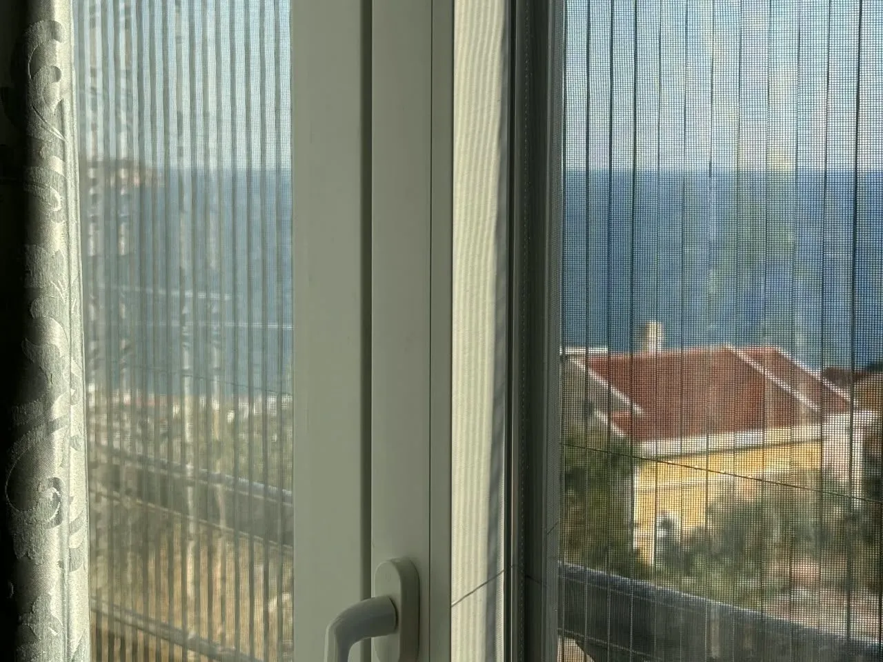 Pogled na more kroz prozor sa mrežicom protiv insekata.