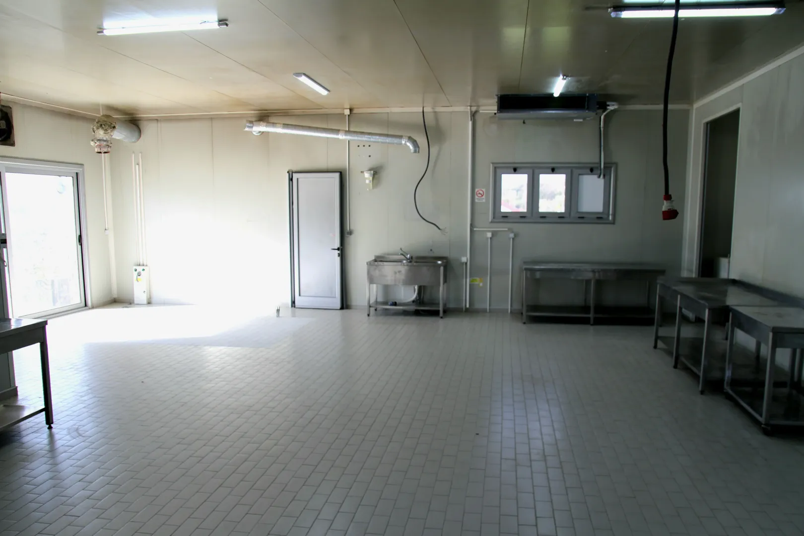 Empty industrial kitchen with stainless steel work surfaces and tiled floors.