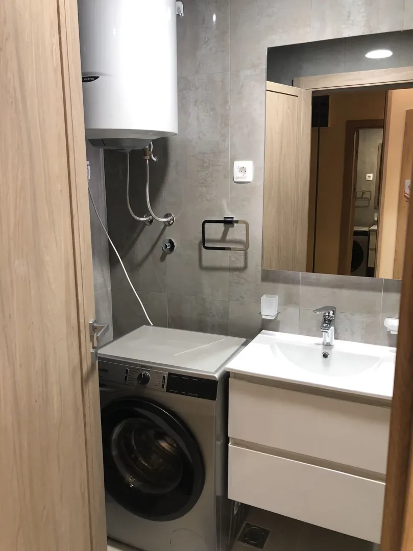 A modern bathroom with a washing machine, sink, and water heater.
