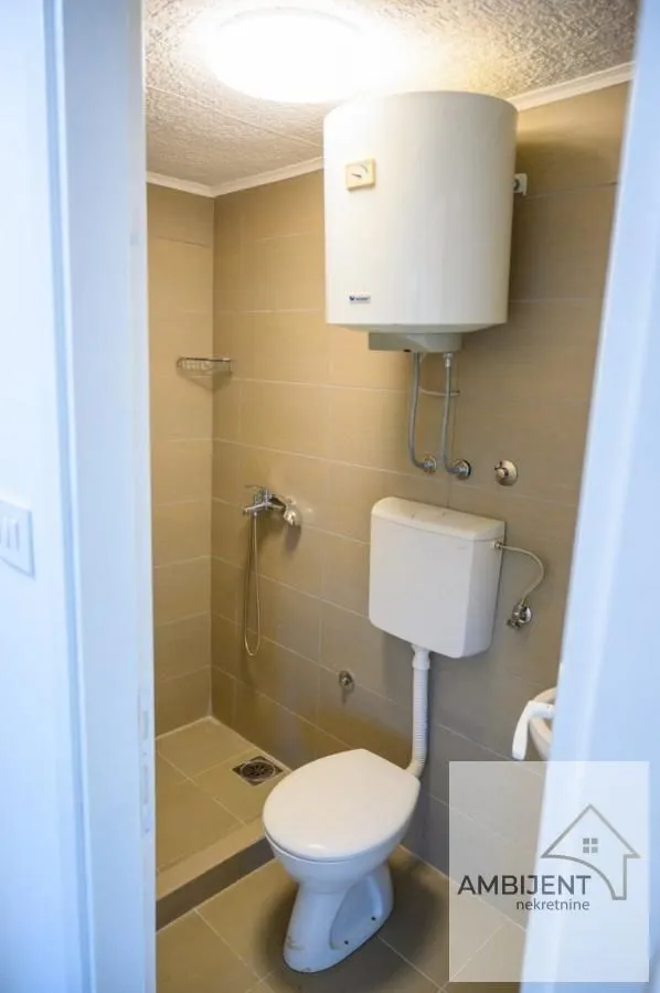 Manje kupatilo sa tuš kabinom, WC šoljom i bojlerom na zidu.