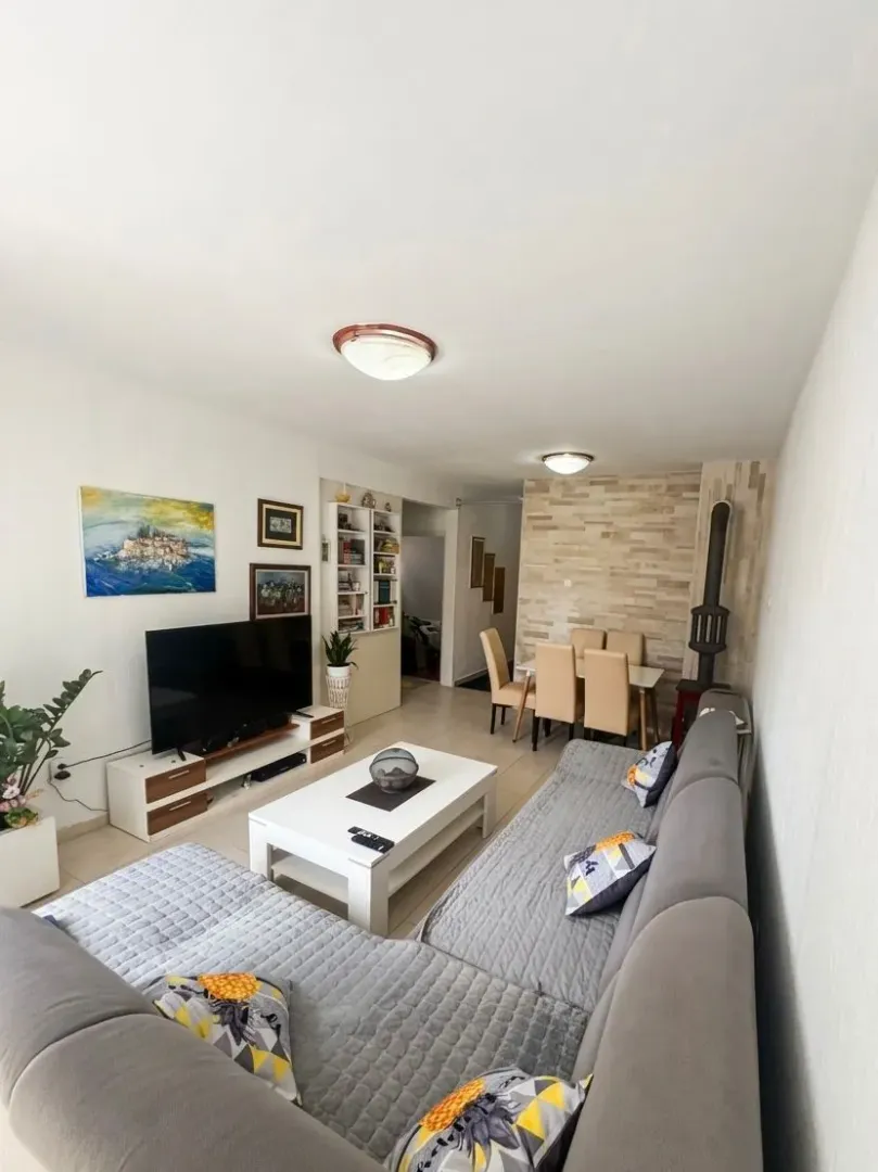 Living room with a sofa, TV, and dining area in the background.