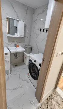 Marble-tiled bathroom featuring a washbasin and a washing machine. - image 3
