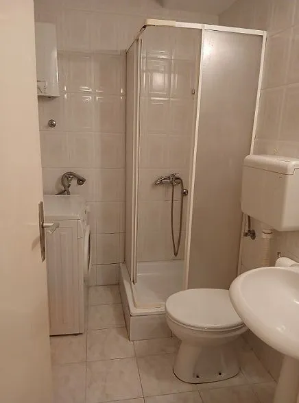 Kupatilo opremljeno tuš kabinom, umivaonikom, toaletom i veš mašinom.