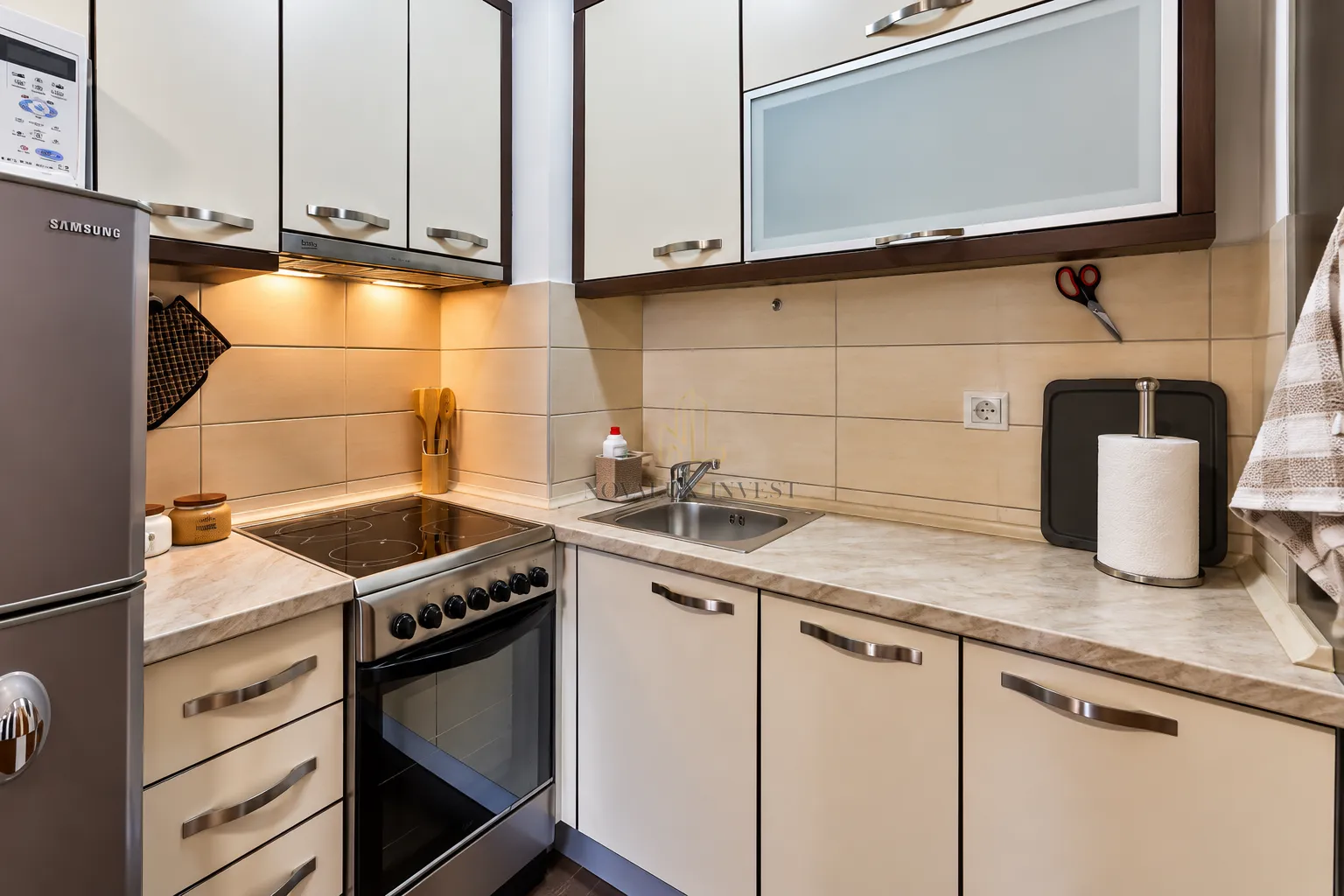 Small kitchen with cream-colored cabinets, built-in oven, and refrigerator.