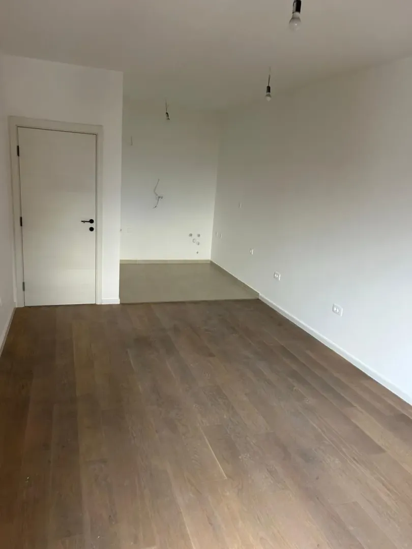 Prazna neuređena prostorija sa drvenim podom i bijelim zidovima.