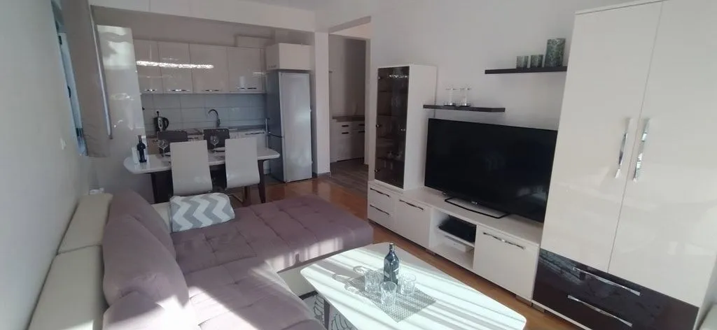 Svijetao dnevni boravak sa ugaonom garniturom i kuhinjom u pozadini.