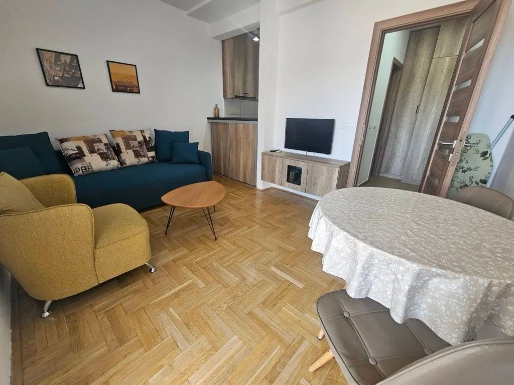 Dnevni boravak sa garniturom, trpezarijskim stolom i kuhinjom u pozadini.