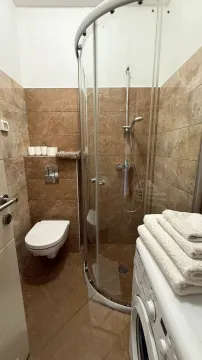 Smaller bathroom with a shower cabin, toilet, and washing machine. - image 8