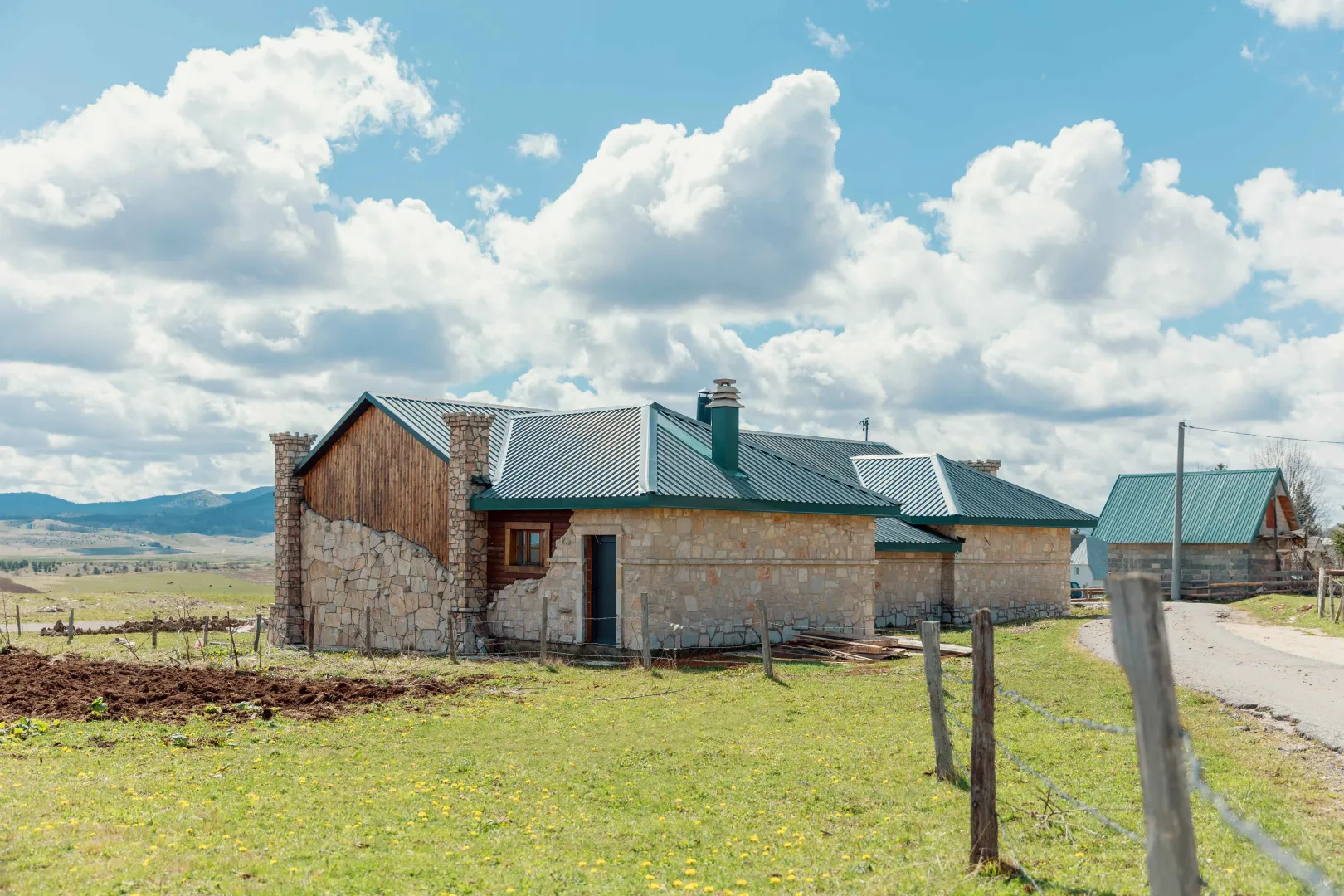 Exterior view of a stone house with a green roof and a yard.