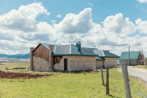 Exterior view of a stone house with a green roof and a yard. - image 24