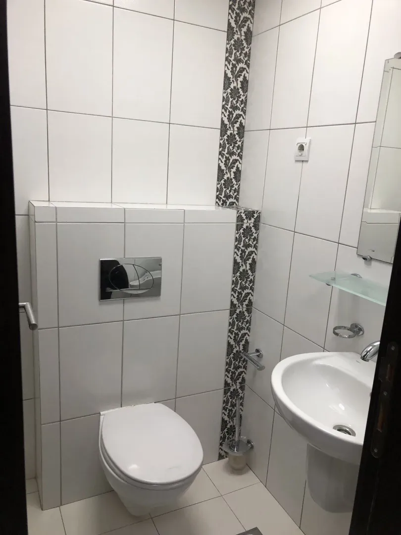 A simple bathroom with white tiles, a toilet, and a sink.