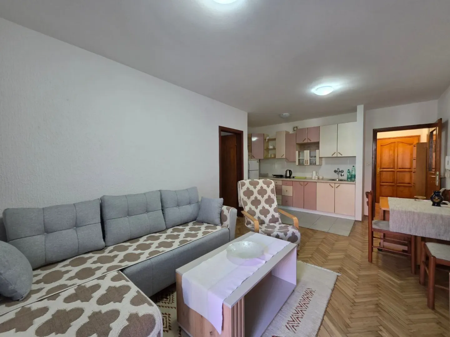 Living room with a sofa, coffee table and a view of the kitchen in the background.