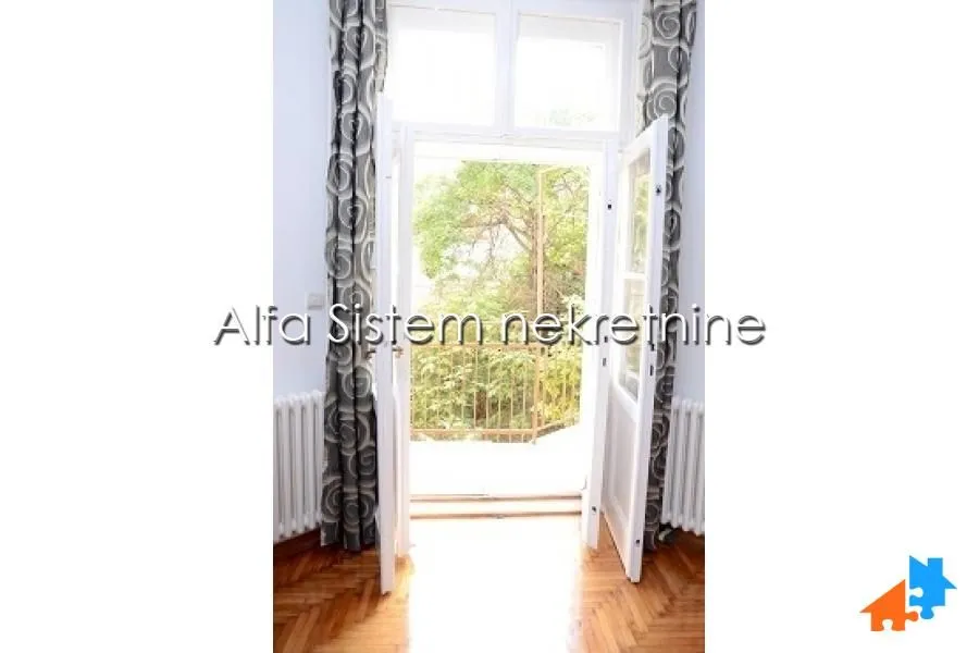 View through open balcony doors with curtains towards the greenery outside.