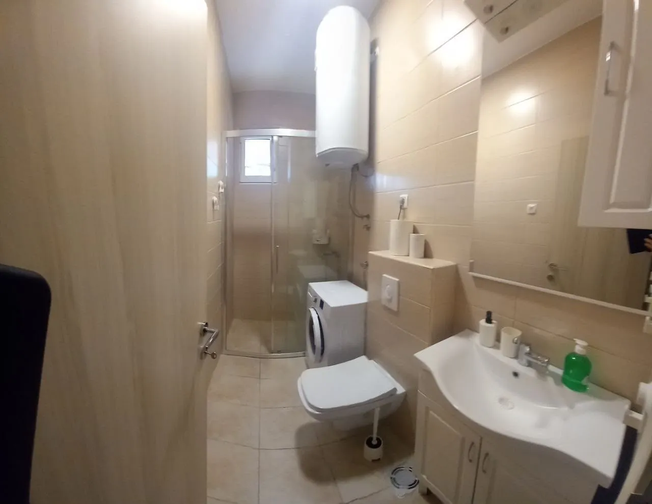 Small bathroom with a shower cabin, washbasin, toilet, and washing machine.