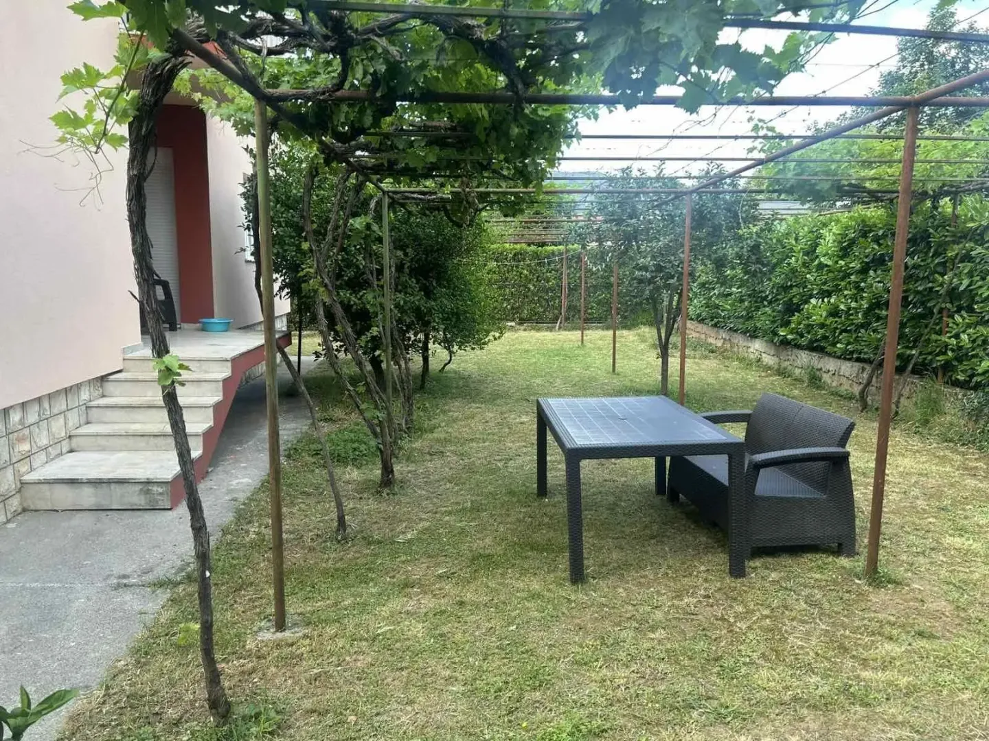 A house yard with outdoor seating under a grapevine trellis.
