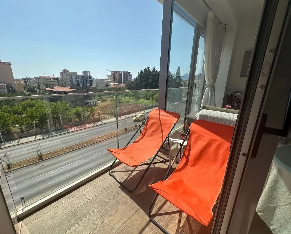 Modern balcony with two orange lounge chairs and a city street view.