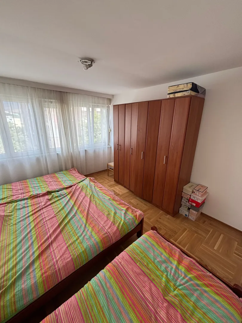 Spavaća soba sa krevetima, drvenim ormarom i prozorom.