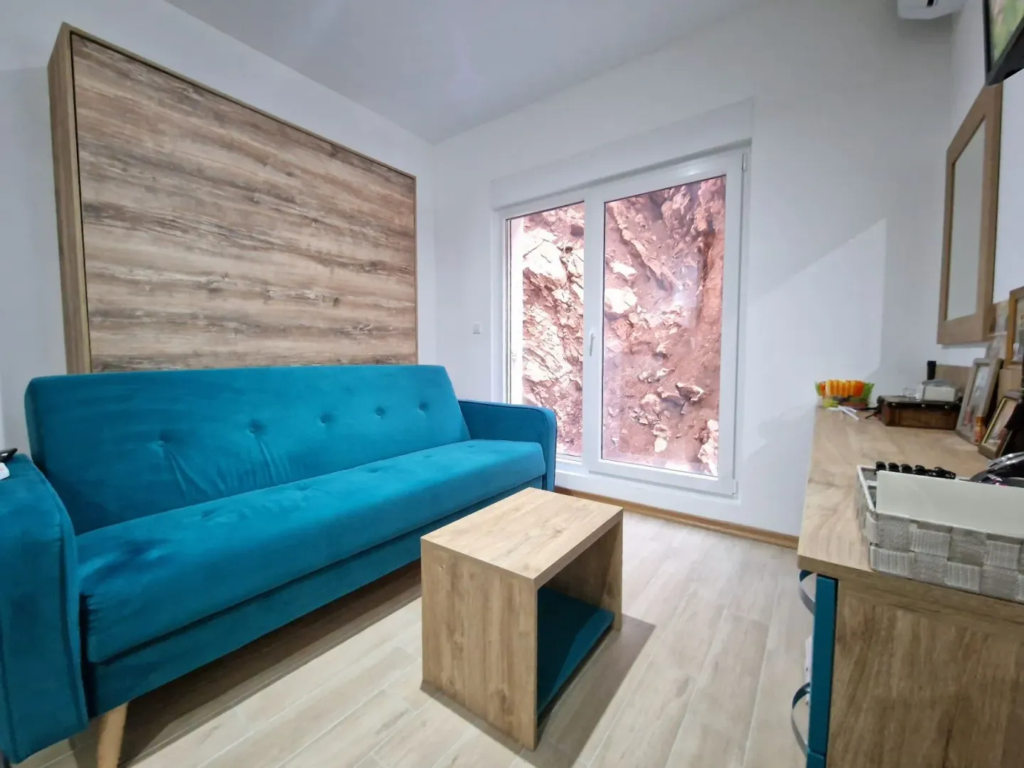 Living room with a blue sofa, wooden coffee table, and a window with a rock view.