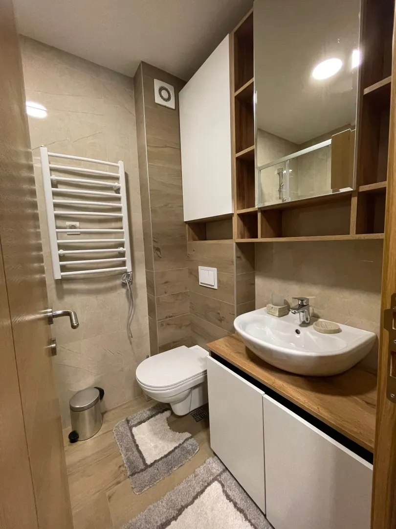 Moderno opremljeno kupatilo sa umivaonikom, WC šoljom i zidnim ormarićem sa ogledalom.