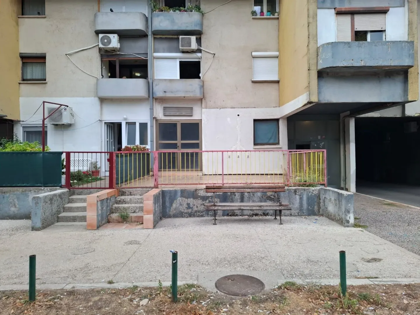 Pogled na spoljašnjost stambene zgrade sa klupom i prilazom.